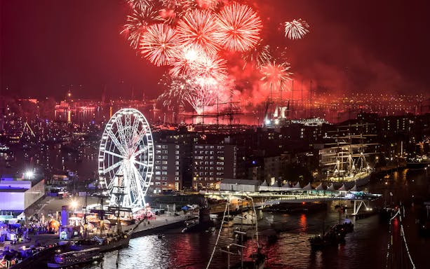 Fireworks over Amsterdam harbor during Sail Amsterdam event with ferris wheel and ships.