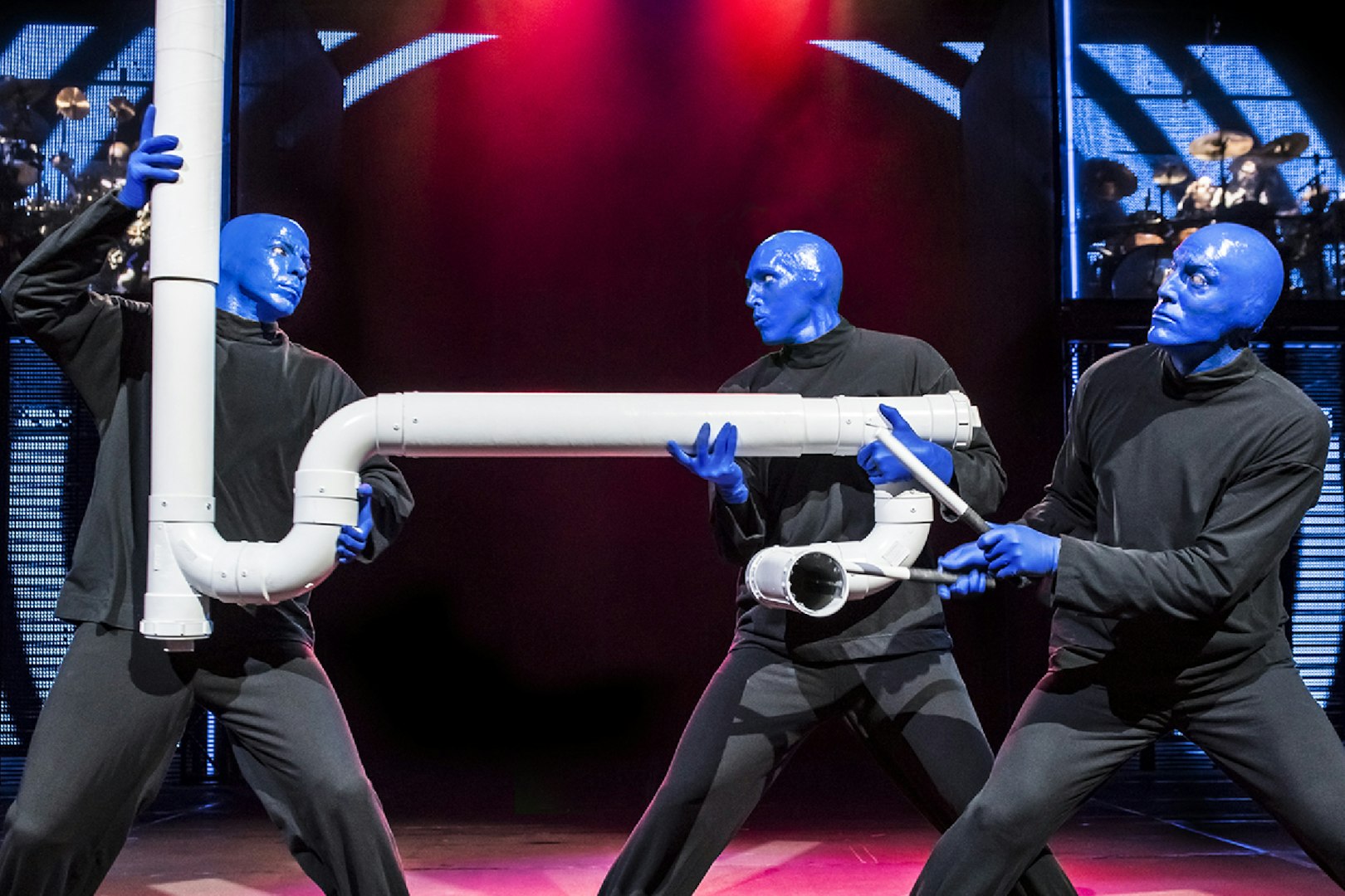 Blue Man Group performers with PVC pipes on stage.
