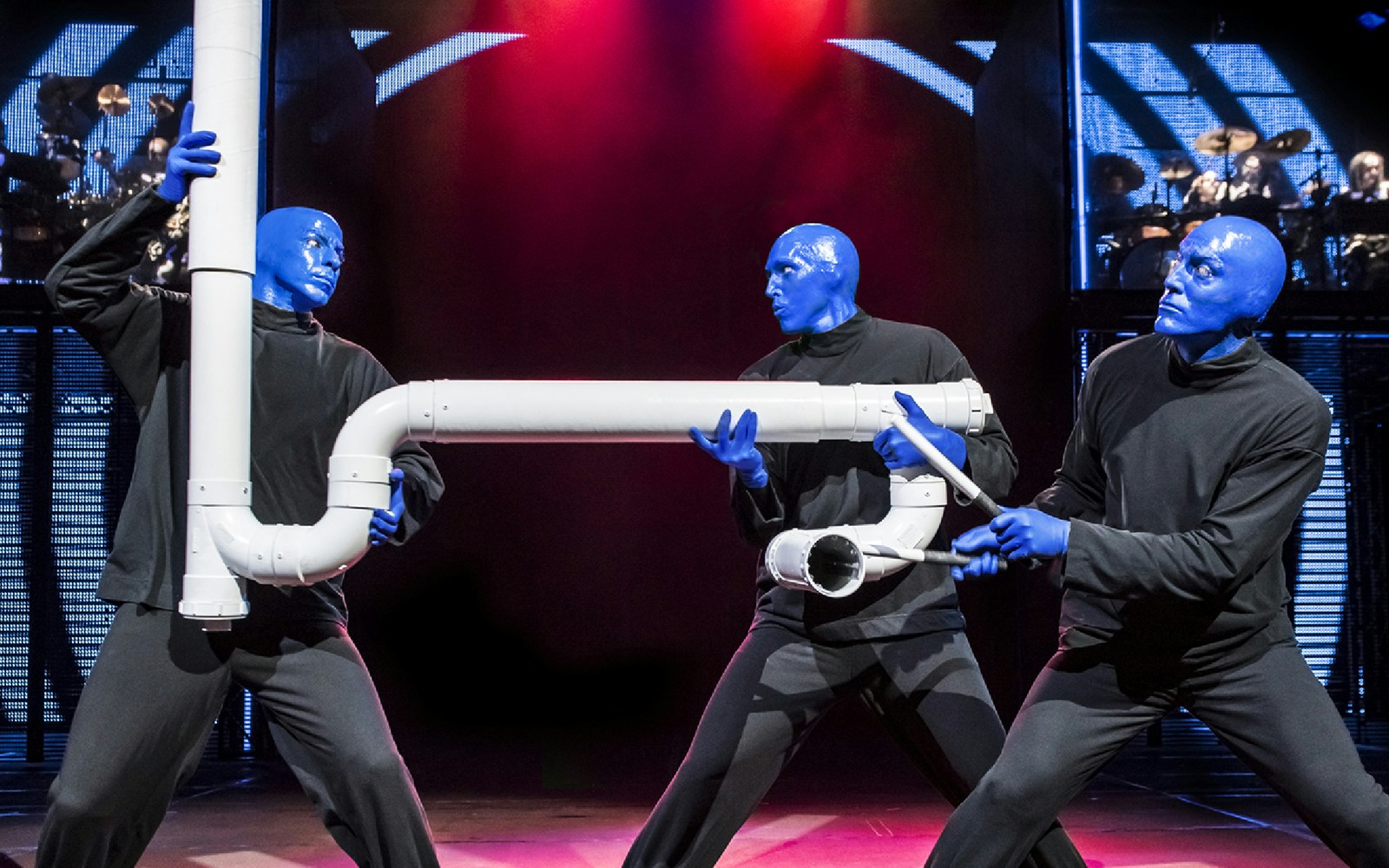 Blue Man Group performers with PVC pipe instruments on stage.