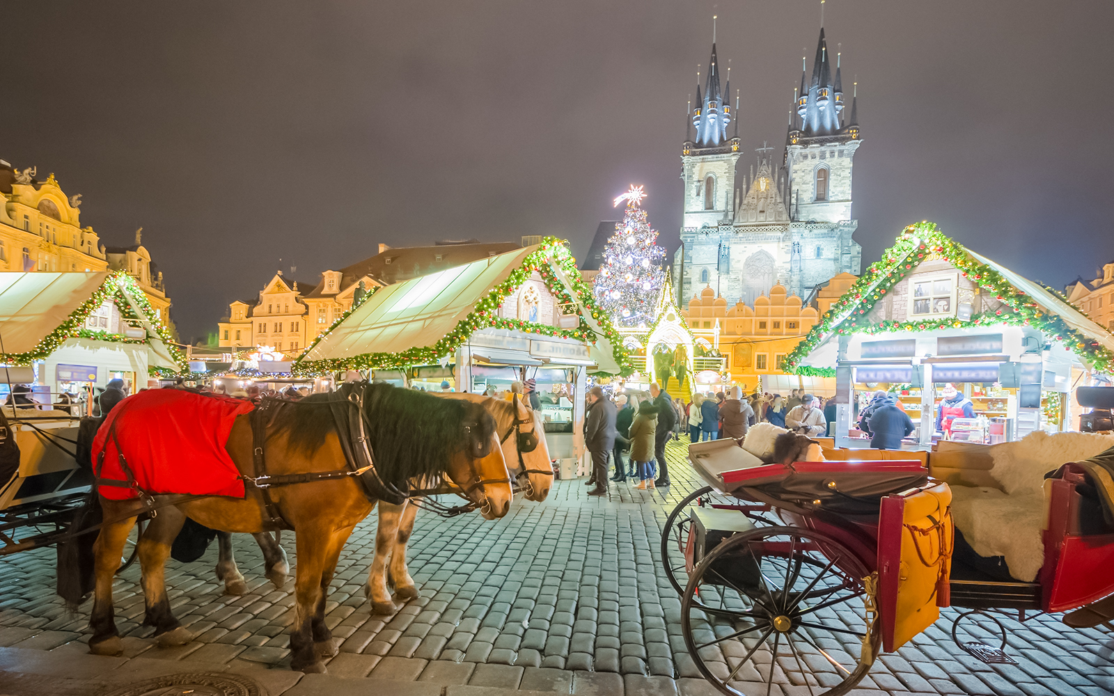 Horse-drawn carriage at Prague Castle Christmas market with festive lights and stalls.