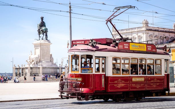 Lisbon tram passing by Praça do Comércio with a statue in the background.