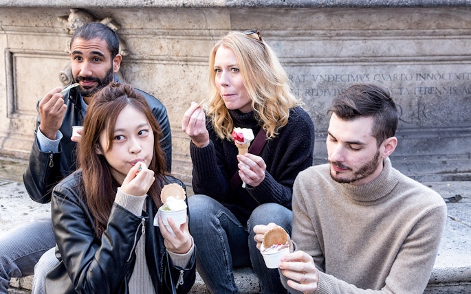 Friends enjoying gelato near a historic stone wall.