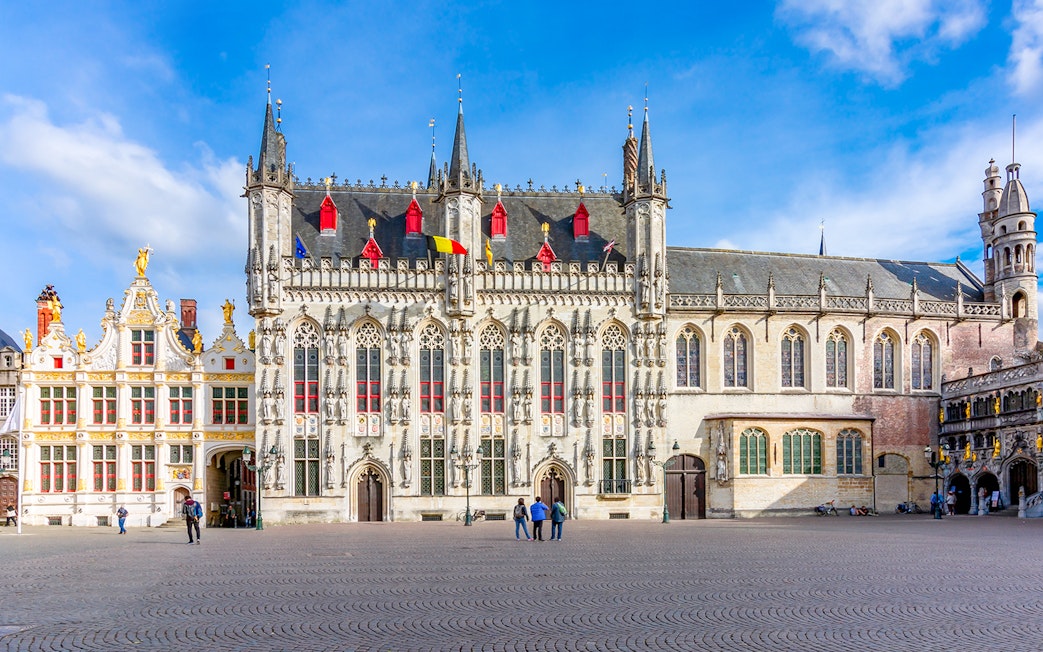 Bruges City Hall exterior with Gothic architecture and flags, Belgium.