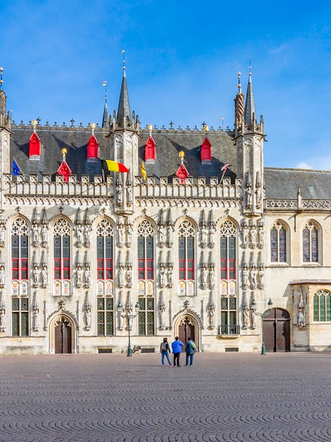 Bruges City Hall exterior with Gothic architecture and flags, Belgium.