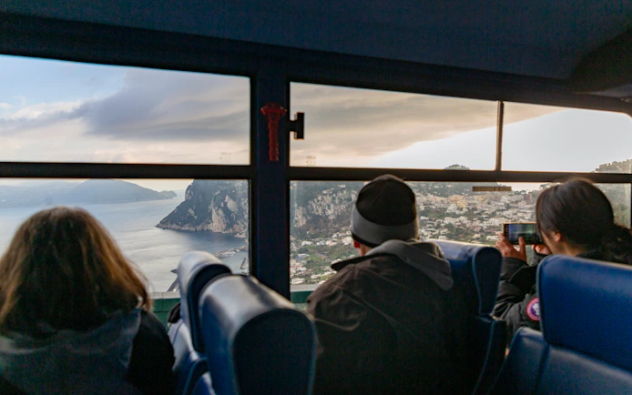 Bus passengers view Capri coastline through window.