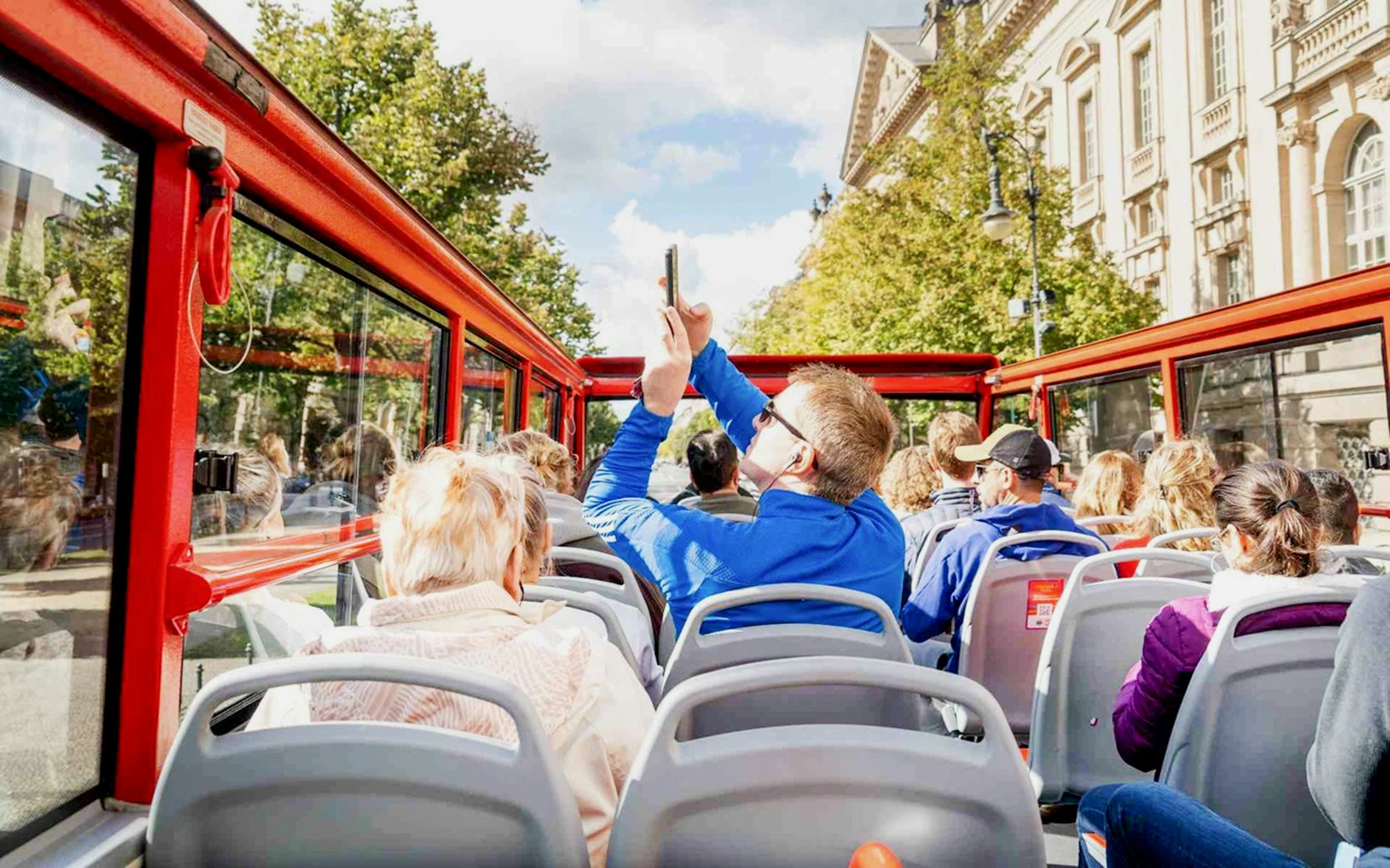 Tourist taking photos on an open-top bus tour in a city.