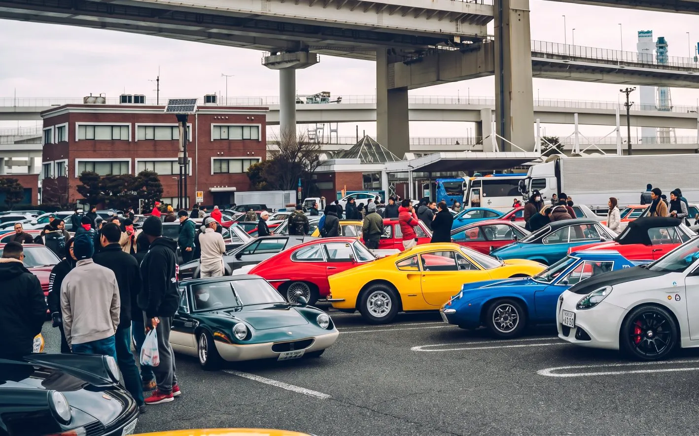 Crowd at Daikoku PA car meet in Tokyo with sports cars on display.