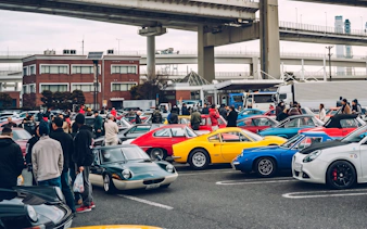 Crowd at Daikoku PA car meet in Tokyo with sports cars on display.