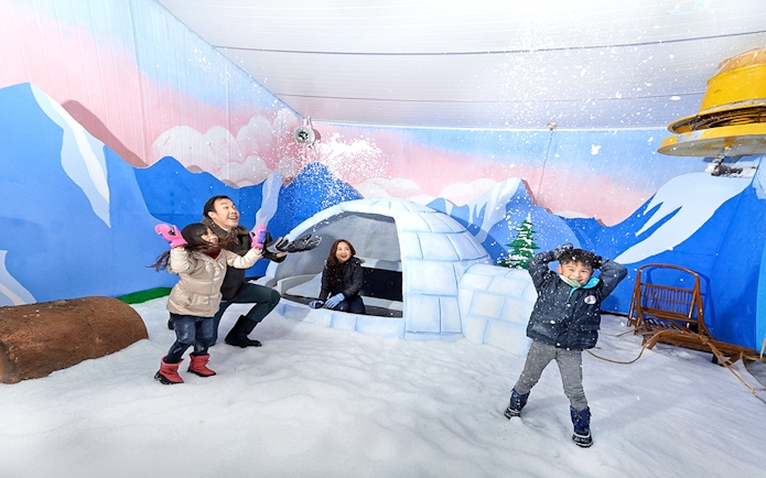 Guests playing in snow inside Singapore Snow City with igloo and mural backdrop.