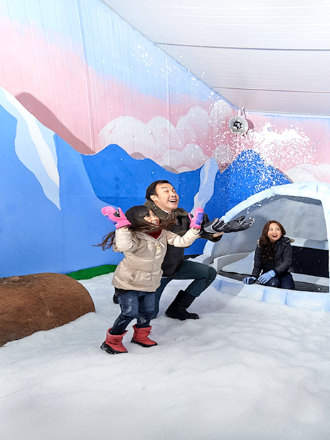 Guests playing in snow inside Singapore Snow City with igloo and mural backdrop.
