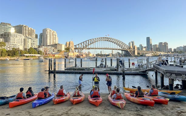 Kayakers gather on Sydney Harbour with city skyline and Harbour Bridge in view.