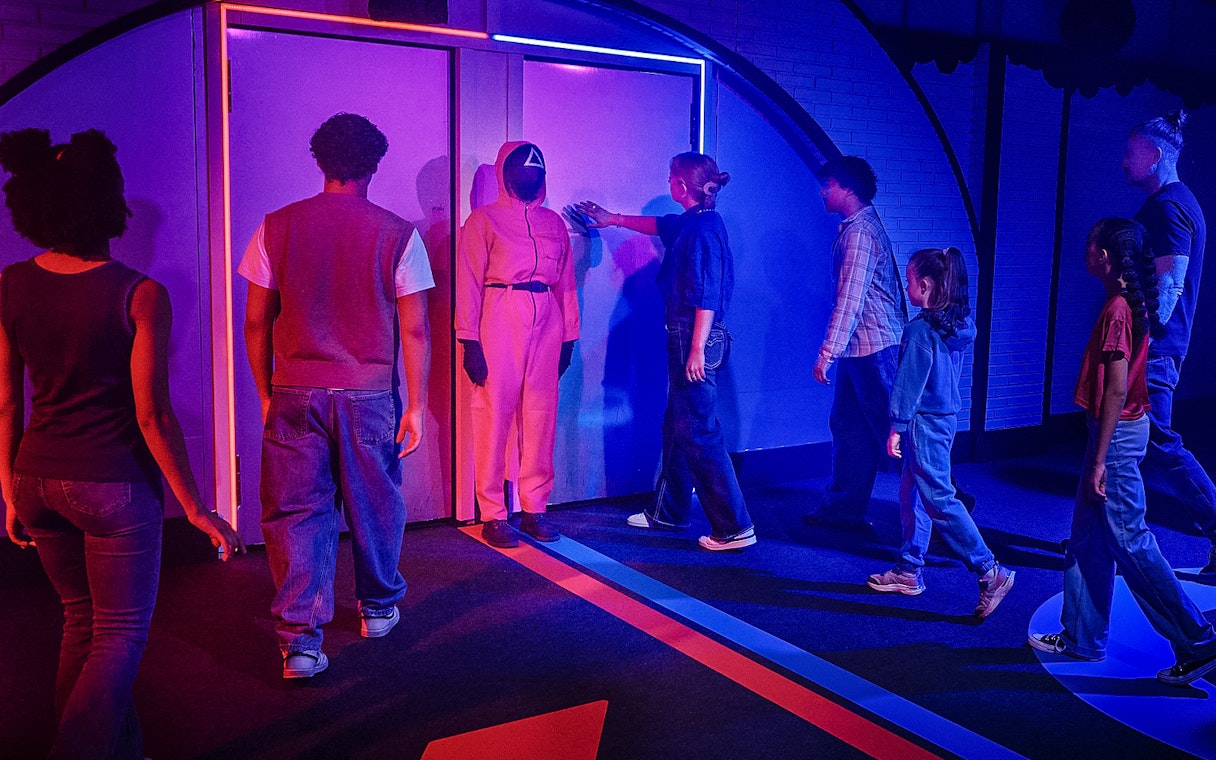 Visitors entering Squid Games experience in London, guided by a masked staff member.