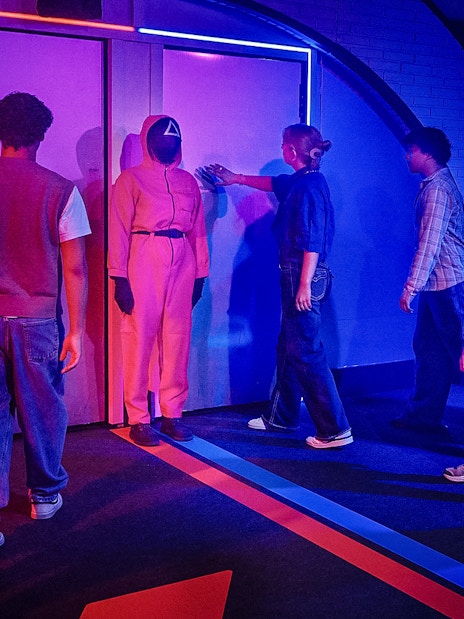 Visitors entering Squid Games experience in London, guided by a masked staff member.