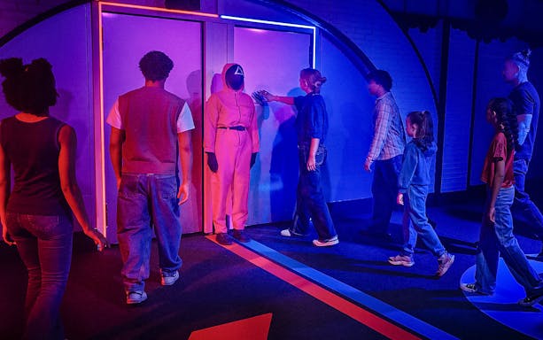 Visitors entering Squid Games experience in London, guided by a masked staff member.