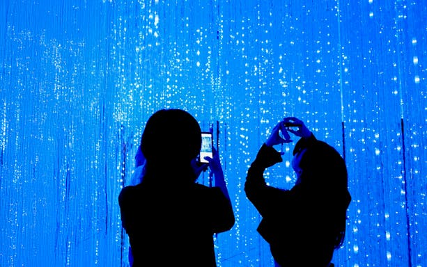 Visitors capturing digital light display at museum installation.