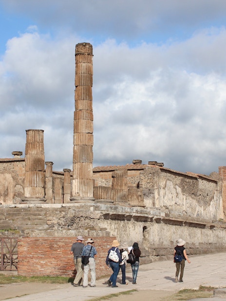 Panoramic view of Pompeii ruins with visitors exploring ancient columns and archway.