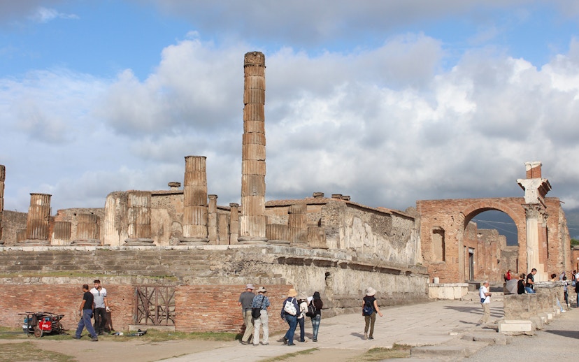 Panoramic view of Pompeii ruins with visitors exploring ancient columns and archway.