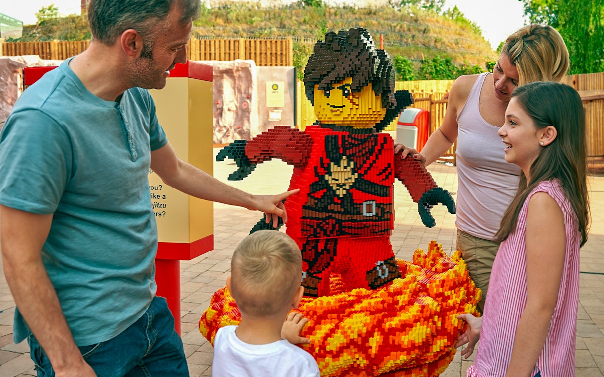 Family interacting with LEGO ninja sculpture at LEGOLAND Windsor Resort.