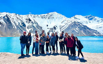 Tourists standing by Embalse El Yeso with snow-capped Andes mountains in the background.