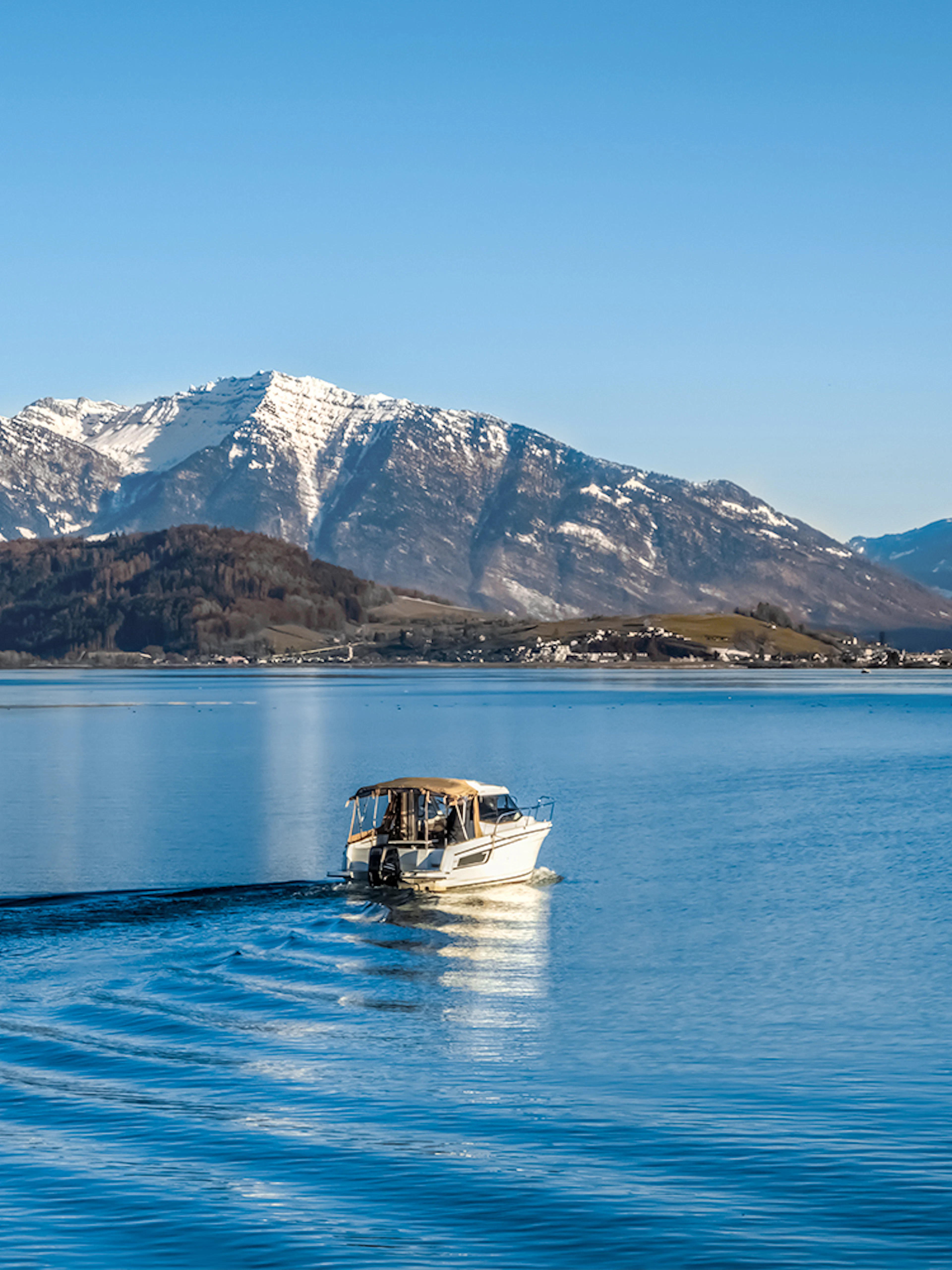 Boat cruising on Upper Zurich Lake with snow-capped mountains in the background.