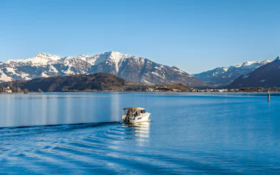 Boat cruising on Upper Zurich Lake with snow-capped mountains in the background.
