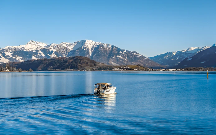 Boat cruising on Upper Zurich Lake with snow-capped mountains in the background.