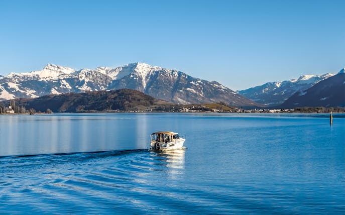 Boat cruising on Upper Zurich Lake with snow-capped mountains in the background.