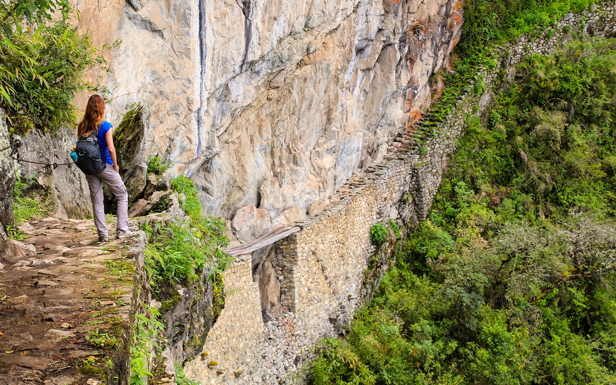Hiker overlooking the ancient Inca Bridge surrounded by lush greenery.
