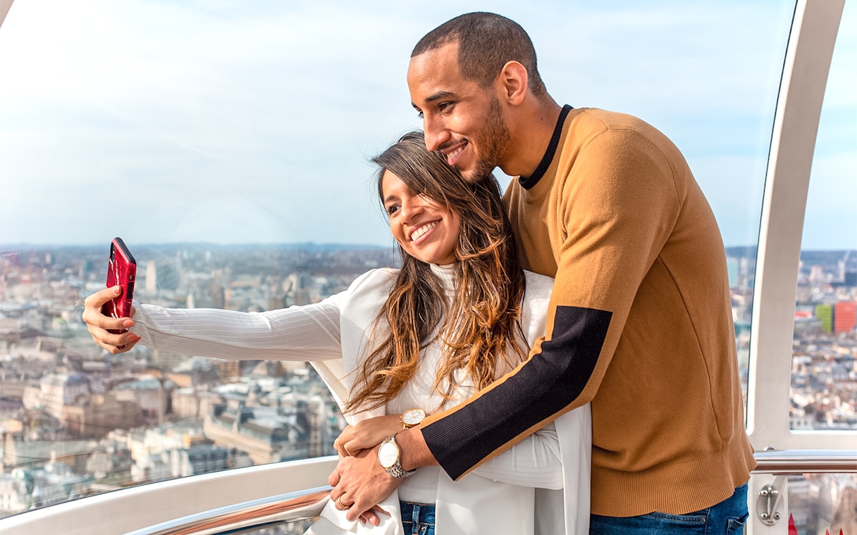 Couple taking a selfie on the London Eye with cityscape view.