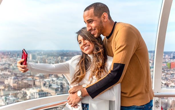 Couple taking a selfie on the London Eye with cityscape view.