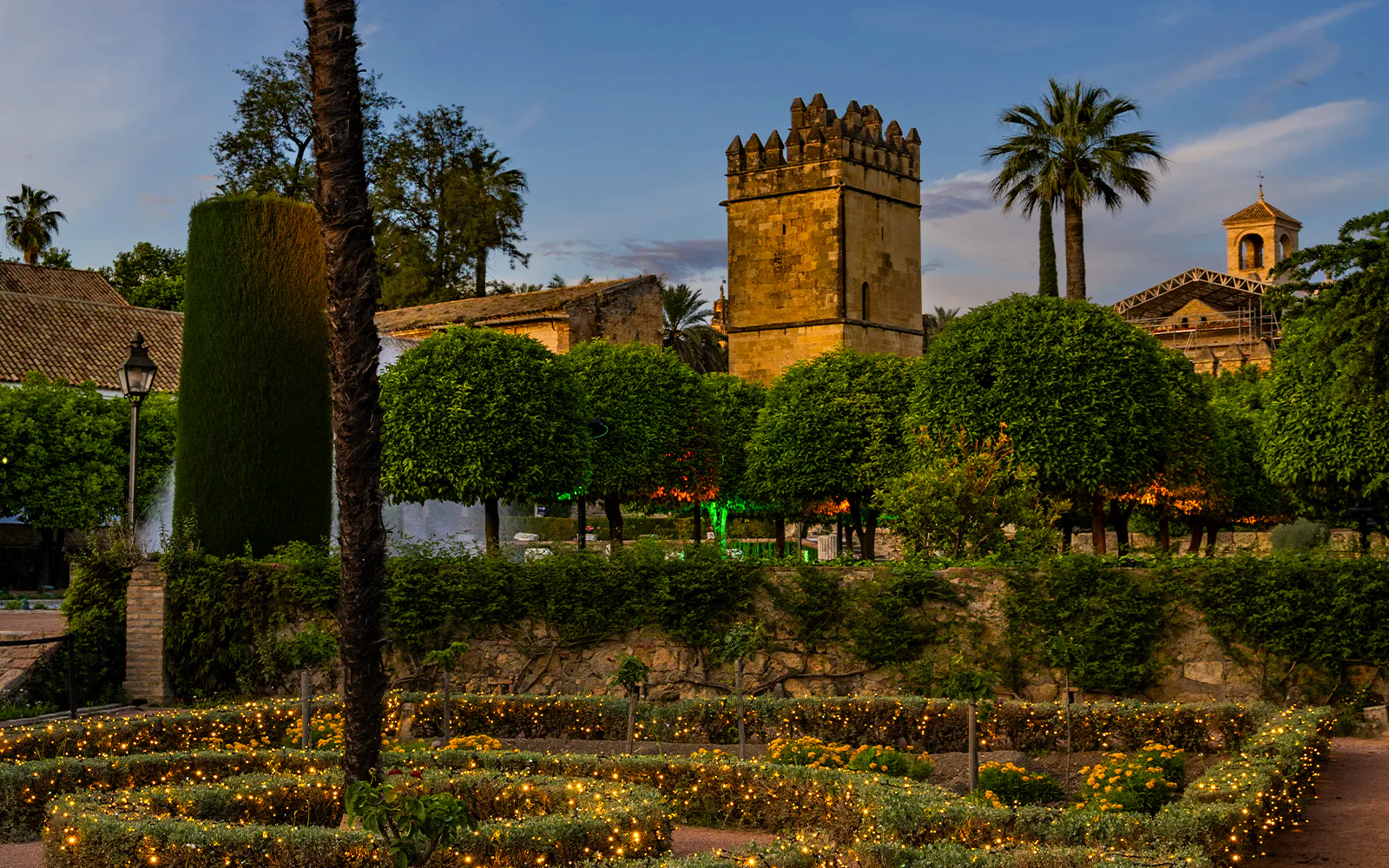 Alcazar of Cordoba gardens illuminated at night with historic tower in view.