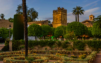 Alcazar of Cordoba gardens illuminated at night with historic tower in view.