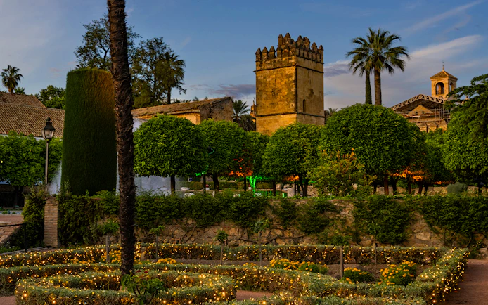 Alcazar of Cordoba gardens illuminated at night with historic tower in view.