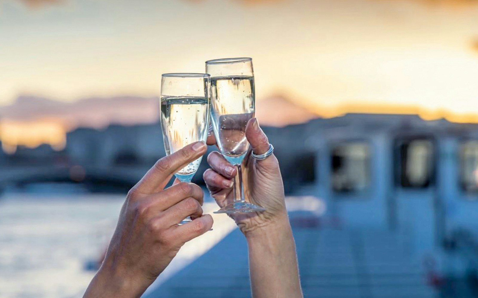 Passengers enjoying a Thames River Evening Cruise at sunset, with a view of London landmarks, while sipping sparkling wine and enjoying canapés