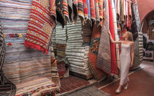 Woman exploring traditional Moroccan rugs in Agadir market.