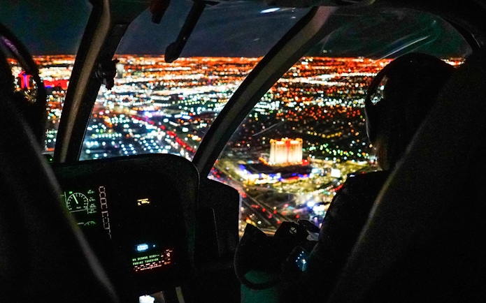 Helicopter cockpit view over city lights at night.