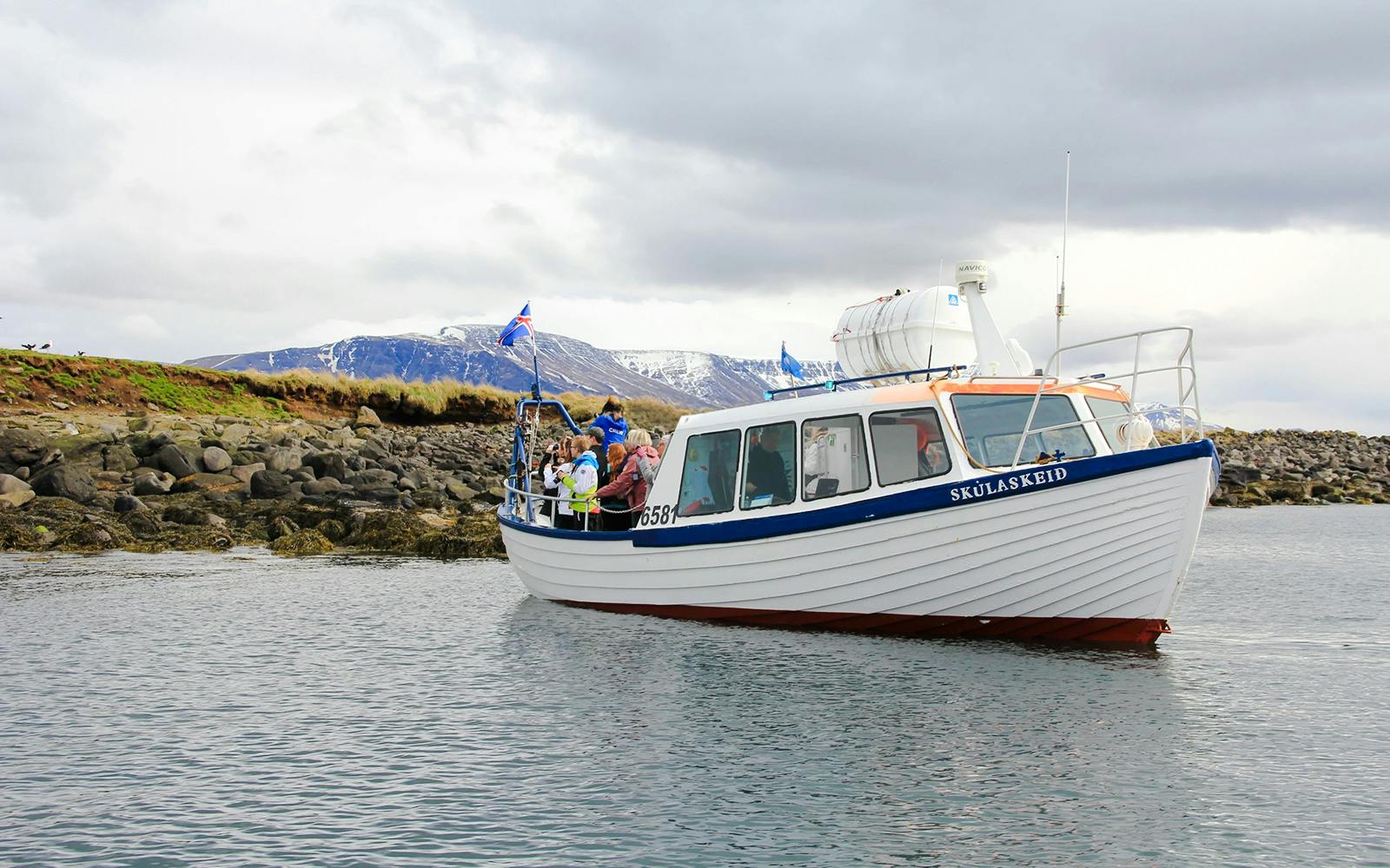 Boat tour with passengers near rocky shore, Reykjavik, Iceland.