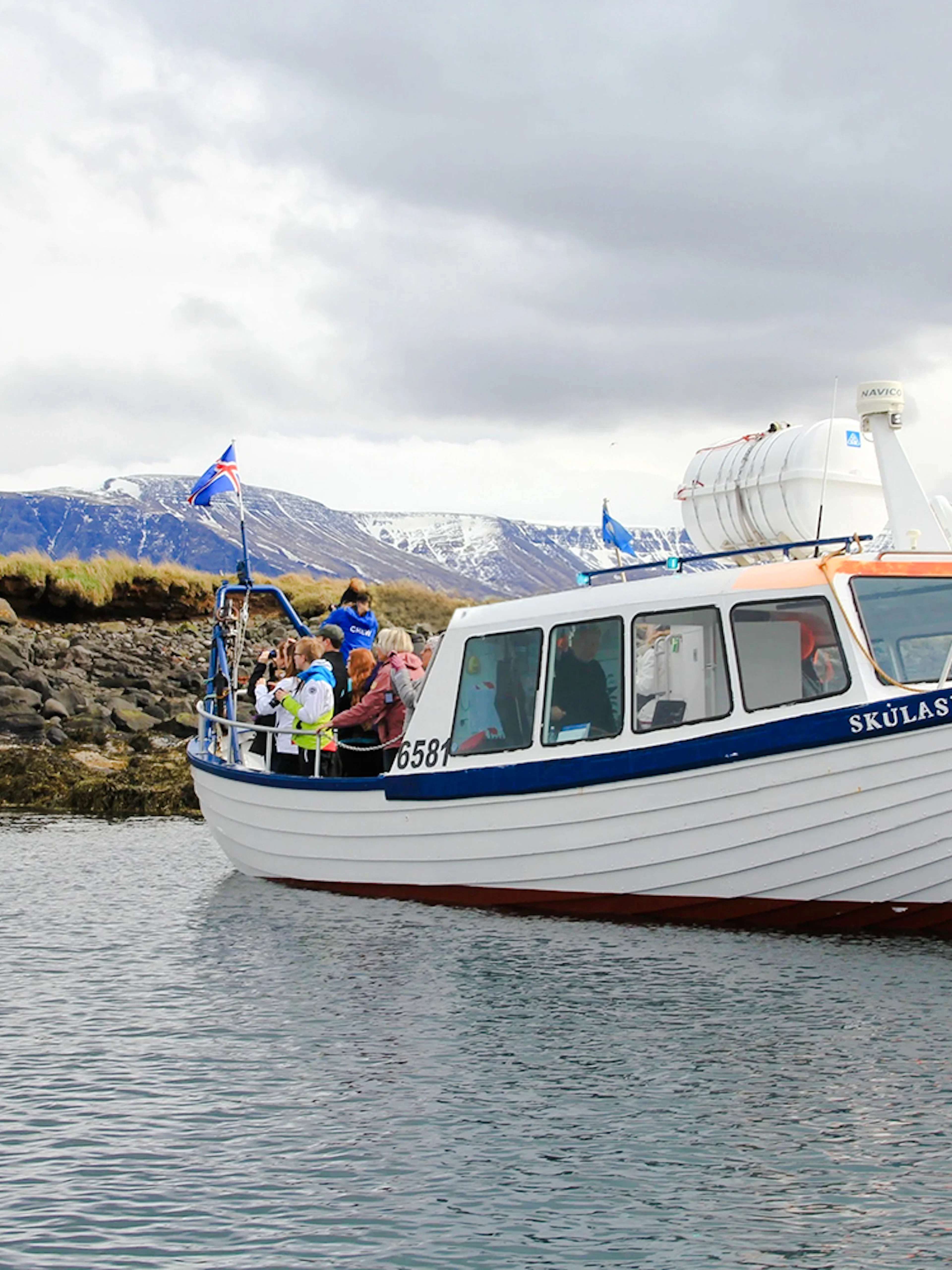 Boat tour with passengers near rocky shore, Reykjavik, Iceland.