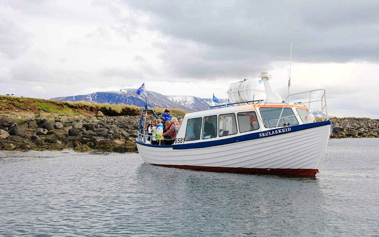 Boat tour with passengers near rocky shore, Reykjavik, Iceland.