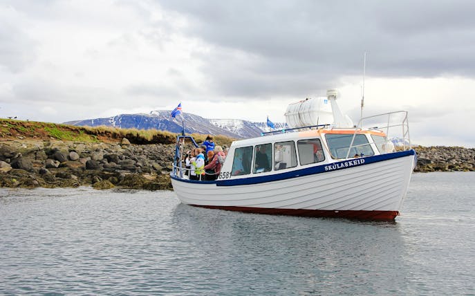 Boat tour with passengers near rocky shore, Reykjavik, Iceland.