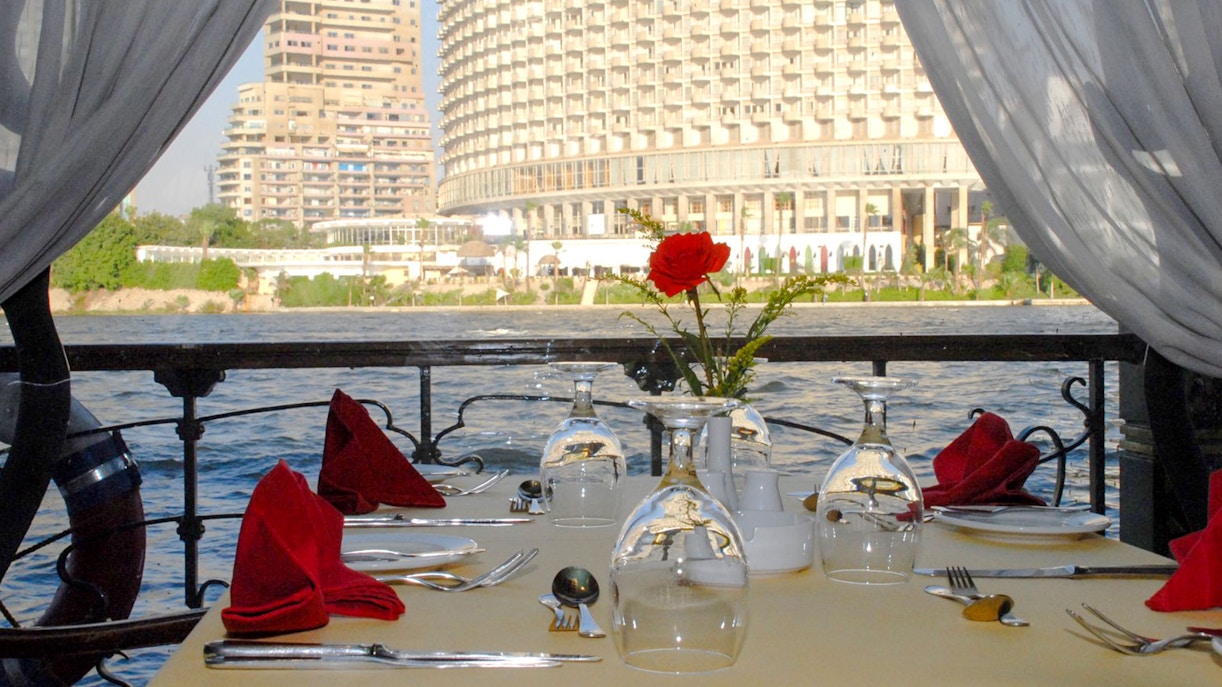 Dining table setup on Luxury Nile Dinner Cruise with cityscape view.