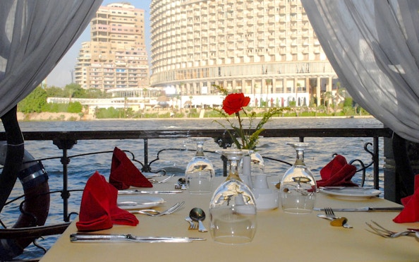 Dining table setup on Luxury Nile Dinner Cruise with cityscape view.