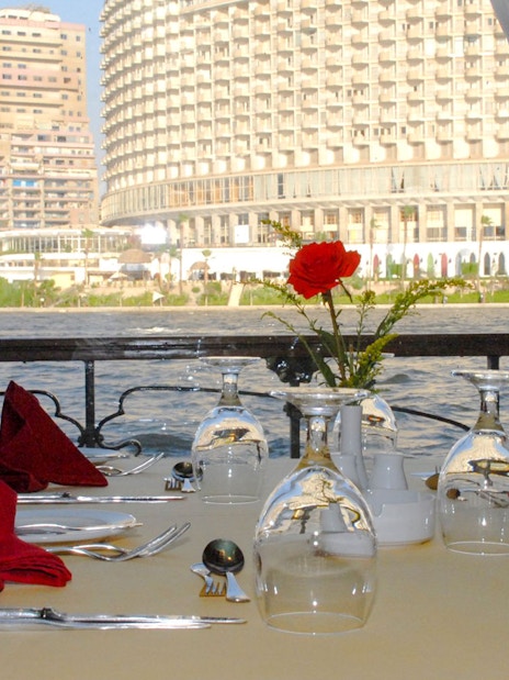 Dining table setup on Luxury Nile Dinner Cruise with cityscape view.