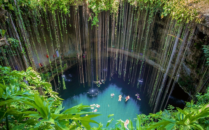 Cenote with swimmers and hanging roots in Yucatan Peninsula, near Chichen Itza, Central America.