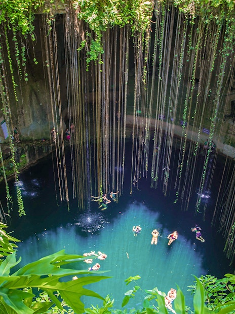 Cenote with swimmers and hanging roots in Yucatan Peninsula, near Chichen Itza, Central America.