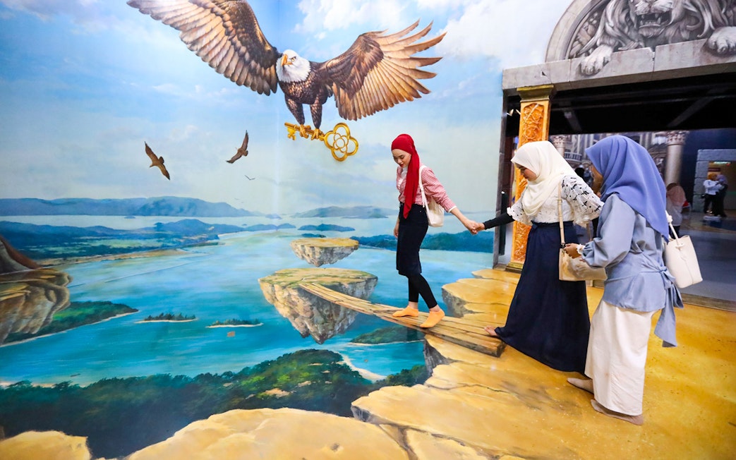 Visitors at 3D Art Langkawi interact with an optical illusion of an eagle and floating islands.