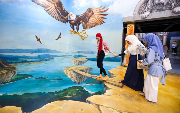 Visitors at 3D Art Langkawi interact with an optical illusion of an eagle and floating islands.