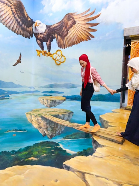 Visitors at 3D Art Langkawi interact with an optical illusion of an eagle and floating islands.
