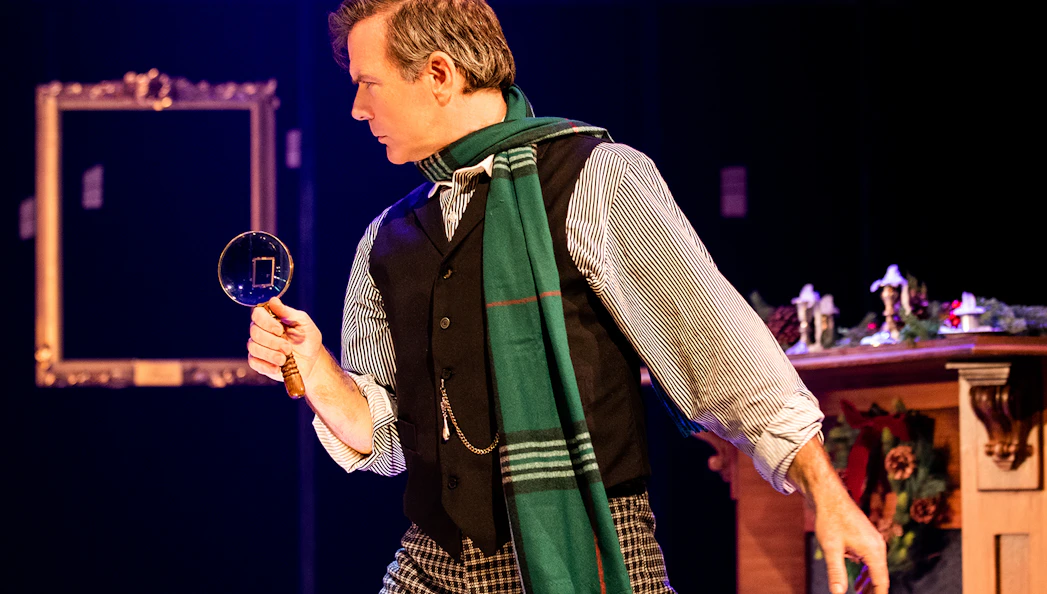Detective with magnifying glass in "A Sherlock Carol" stage scene.