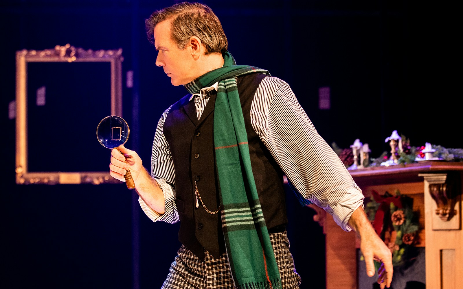 Detective with magnifying glass in "A Sherlock Carol" stage scene.